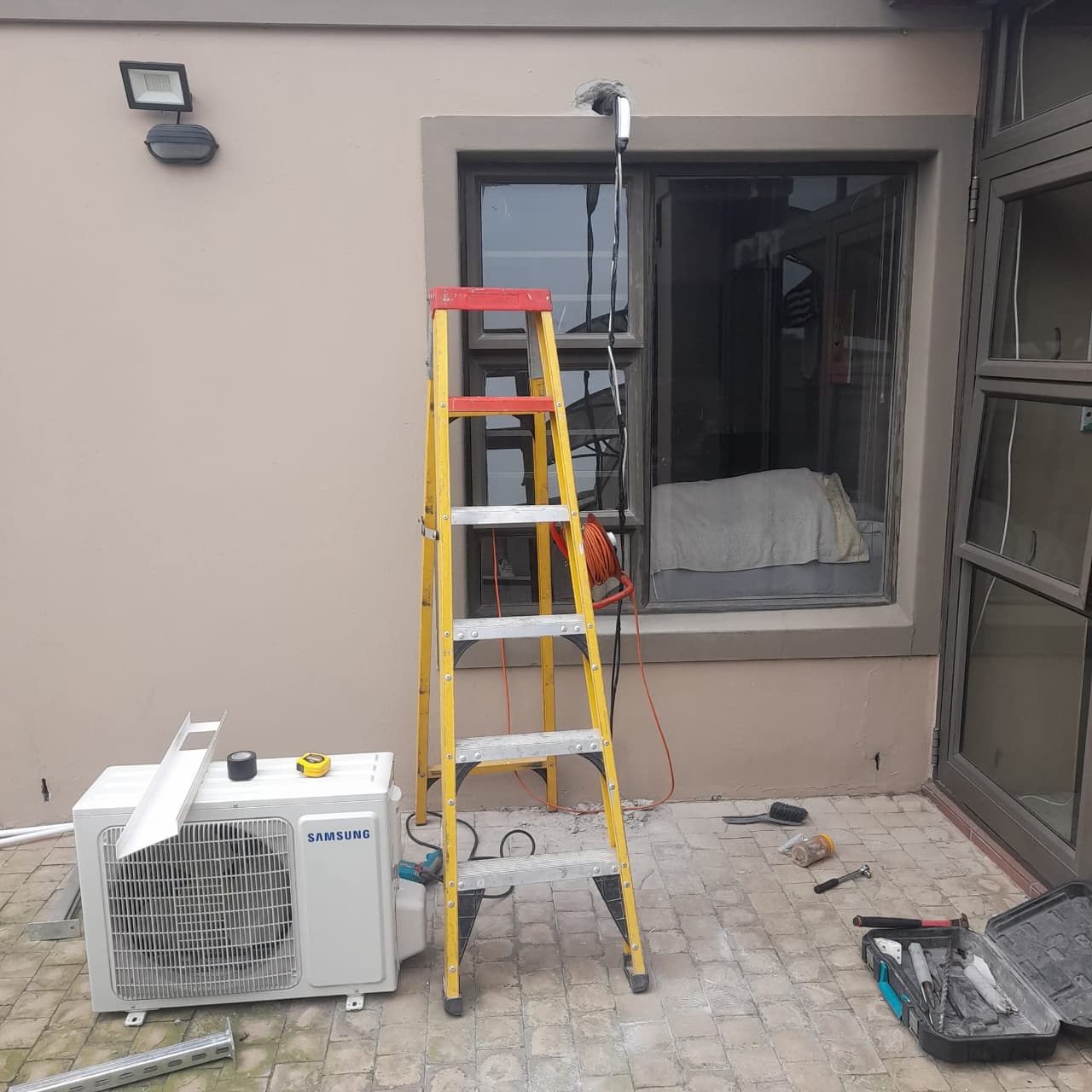 Samsung outdoor air conditioning unit on a patio ready for installation, with ladder and tools set up