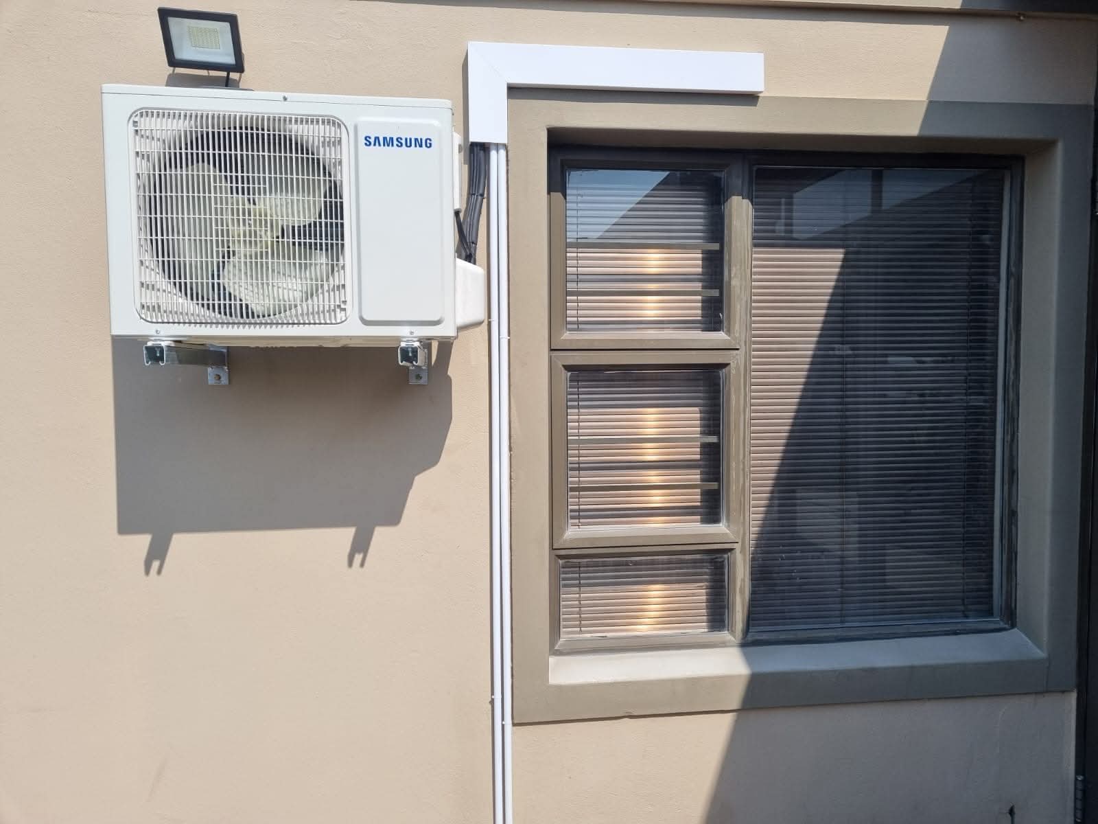 Samsung outdoor air conditioning condenser unit wall-mounted beside a window