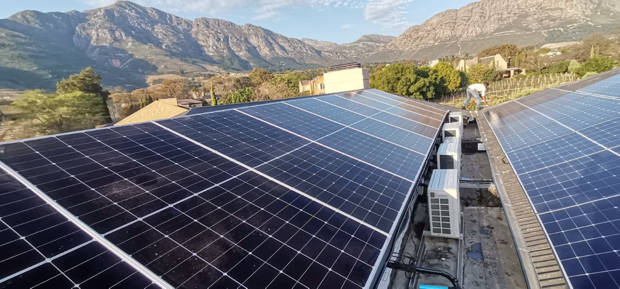 Large solar panel installation on a rooftop with a mountain backdrop, completed by Air Tech Solution Systems